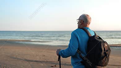 Active old man backpacker going Scandinavian walking stick at sea beach sky landscape closeup