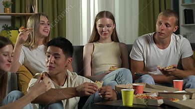 Medium video of a group of teens, young people, friends sitting on a couch and floor around the table, eating pizza