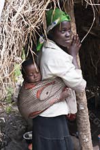 African mother with baby in sling in front of hut, Uganda