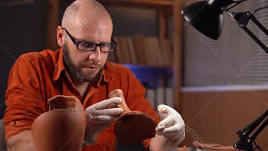 Male archaeologist working in office at night studying artifact of ancient civilization. Concept of a find at excavation