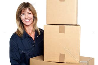 Cheerful delivery woman carrying sealed cartons