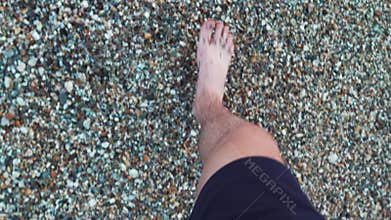 Man walking barefoot on a rocky beach near the sea in Greece