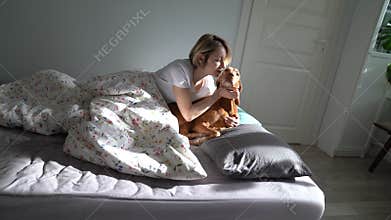 Single middle-aged woman playing and cuddling with beloved dog in bed after waking up