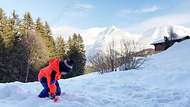 Boy play outside and throw snow with shovel over mountains