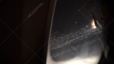 POV of a passenger looking through airplane or flight window during flying in rain at night. Appears to be inflight journey