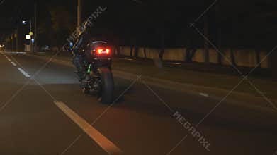 Motorcyclist racing his motorcycle on evening city. Man riding on modern sport motorbike at night street of town. Guy