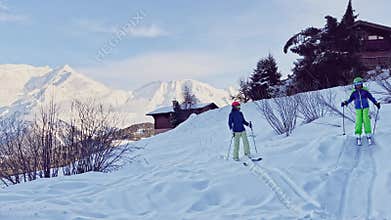 Mother with child go downhill ski in to the hotel at mountains