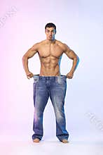 Young man showing how much weight he lost with big jeans. Fat to fit concept. Fitness poster
