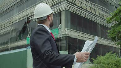 Portrait successful handsome engineer, architect, builder, businessman in white helmet, in suit, holding project in his