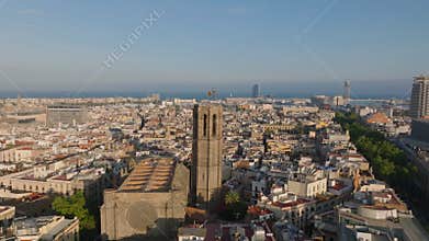 Forwards fly above old town quarter at golden hour. Fly over Basilica de Santa Maria del Pi tower with Catalan flag on