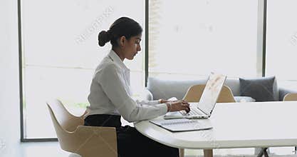 Concentrated young Indian woman work on laptop sitting in office