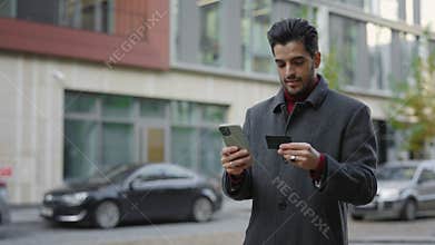 Happy Male Multicultural Shopper Embraces Online Purchases. Man Using Smartphone and Credit Card for Online Shopping