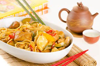 Stir-fried noodles with chicken and vegetables served in a bowl, over bamboo mat with tea