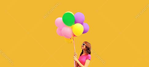 Summer colorful image of happy smiling young woman looking up at multicolor balloons on orange background