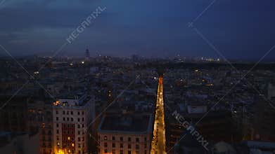 Forwards fly above evening city. Street glowing into night. Buildings in urban borough of metropolis. Barcelona, Spain