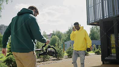Videographer shoots video featuring african man in yellow hoodie and headphones in courtyard of residential complex