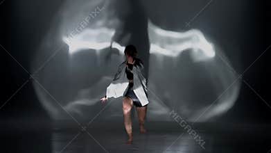 Young woman wearing a top, shorts and a shirt performing contemporary dance under the glare of the light in the studio