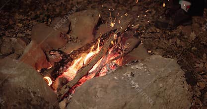 Close-up. A fire surrounded by stones is burning. Firewood is added to the fire and sparks fly in the darkness