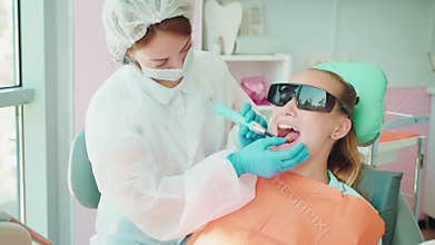 dentist installing dental filling in tooth of teenage girl, illuminating blue light, curing caries