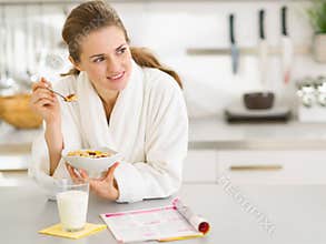 Thoughtful woman in bathrobe eating breakfast