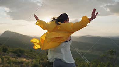 A girl on top of a mountain raises her hands to the mountains.