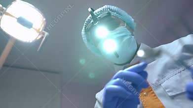 Concentrated professional dentist adjusting dental headlight leaning to camera with instruments. Portrait of confident