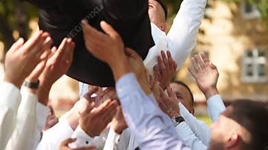 Groomsmen toss groom in the air. Man flexing and having fun with best friends on wedding day in park. Cheerful guys