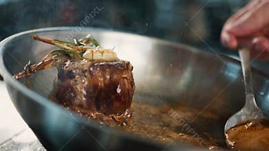 Close-up: Chef pouring sauce over filet mignon while cooking