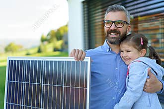 Father with his little daughter near their house with solar panels. Alternative energy, saving resources and sustainable