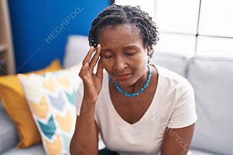 Middle age african american woman stressed sitting on sofa at home