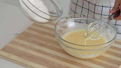 Woman adds flour to the eggs beaten with sugar for the preparation of the cake