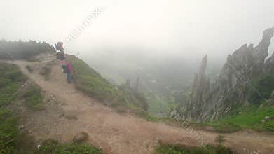 Aerial view of three hikers walk along foggy mountain trail with strong wind.