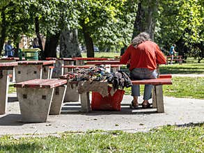 Man sitting alone on a bench in a public park with handmade items beside him