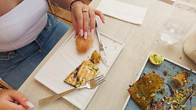 Woman Picking Up Bread To Eat With Fish At Restaurant