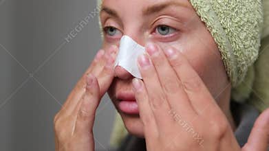 Woman applies nose strip for blackhead removal as part of facial cleansing routine.