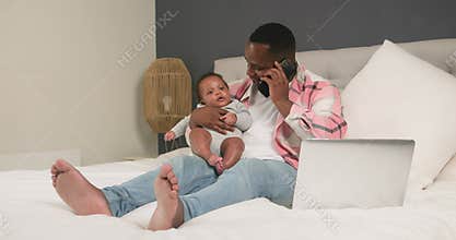 Working From Home Dad Balances Business Call and Baby Care on Laptop in Cozy Bedroom Setting