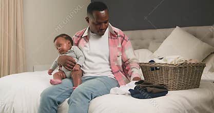 Loving Father Folds Laundry While Holding His Baby: A Tender Moment of Childcare and Family Life in the Bedroom