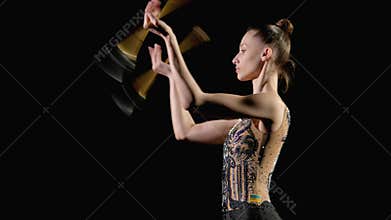 Side view of elegant rhythmic gymnast performing small throw with clubs