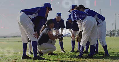 Huddling softball team listening to coach kneeling with clipboard in outfield, blue jerseys, gloves