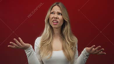 Woman with long blonde hair raising both hands in a shrug gesture in a photo studio; confusion frustration