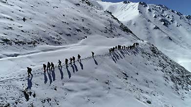 Hikers walk along narrow snowy mountain trail in clear winter weather drone view