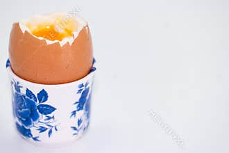 Soft boiled egg served in a floral patterned egg cup on a simple white background during breakfast time