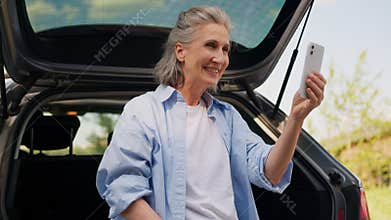 Happy smiling elderly senior mature Caucasian woman tourist automobile driver female blogger influencer use mobile phone