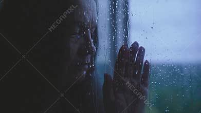 Unhappy elderly mature woman crying standing looking at window rain drops falling water drip flow down the glass, mood