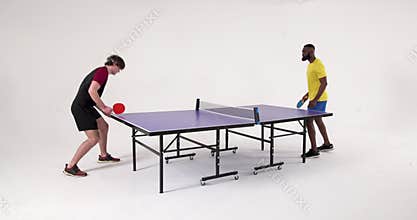 Playing table tennis, two men competing in match in studio setting