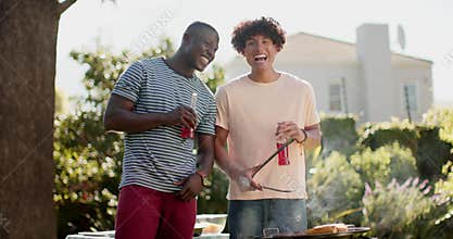 Grilling food, two multiracial male friends smiling and enjoying drinks at outdoor barbecue