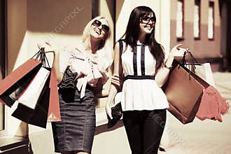 Two happy fashion women with shopping bags walking in city street