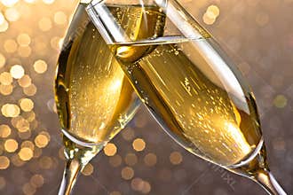 Detail of a champagne flutes with golden bubbles on light bokeh background