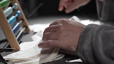 A man counts expenses on a wooden abacus. A man keeps accounts.