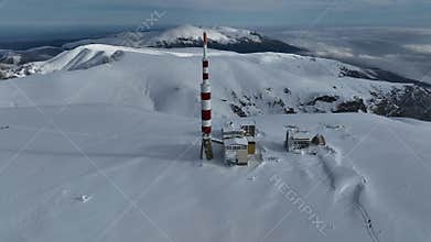 Aerial view of alpine mountain range covered in snow, with snow-capped peaks and a communications tower